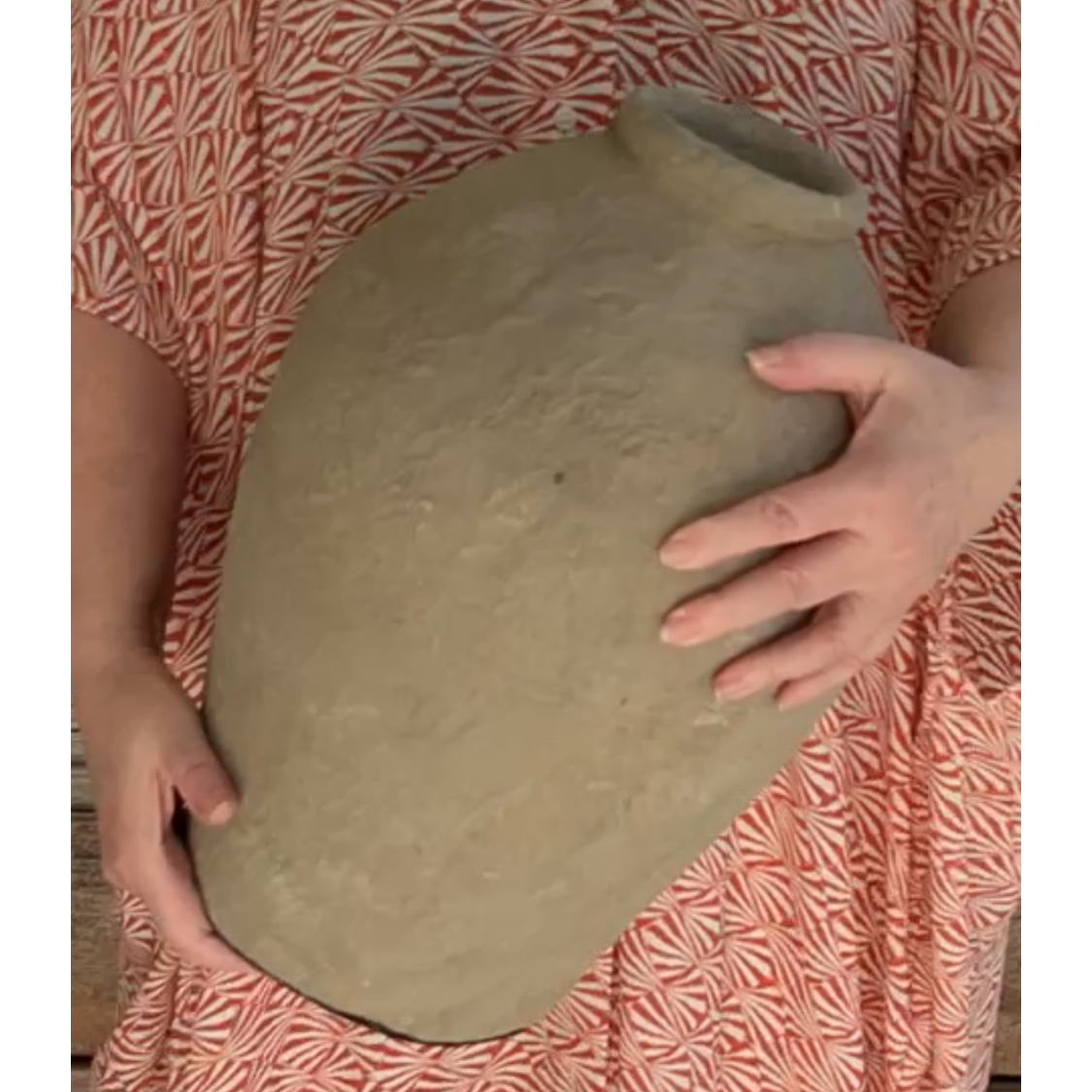 Person holding a pot that looks like stone, against a patterned garment.