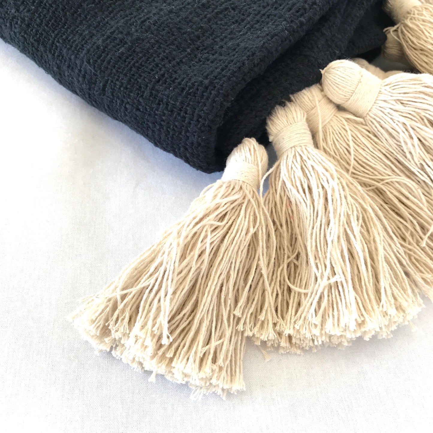 Close up of a black cotton woven blanket showing the weave and natural coloured cotton tassels.