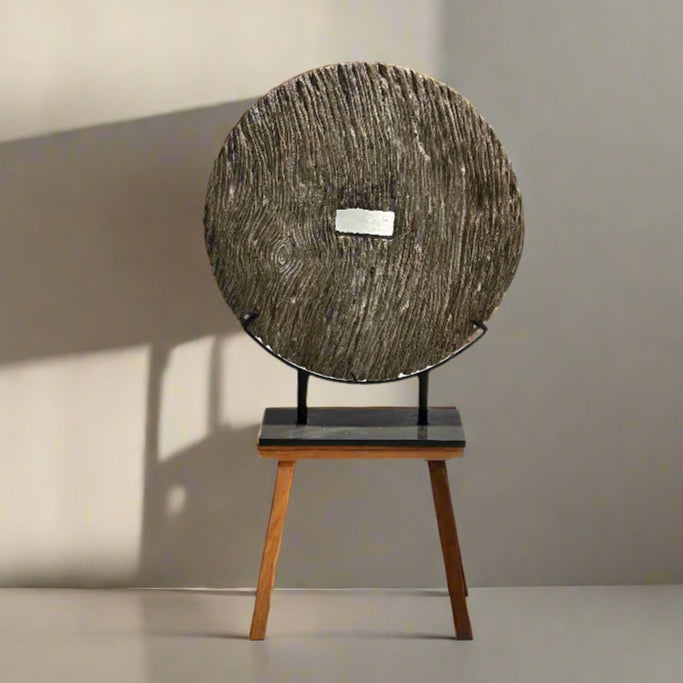 Indonesian hand carved 80cm wide timber wheel on metal stand against a beige wall