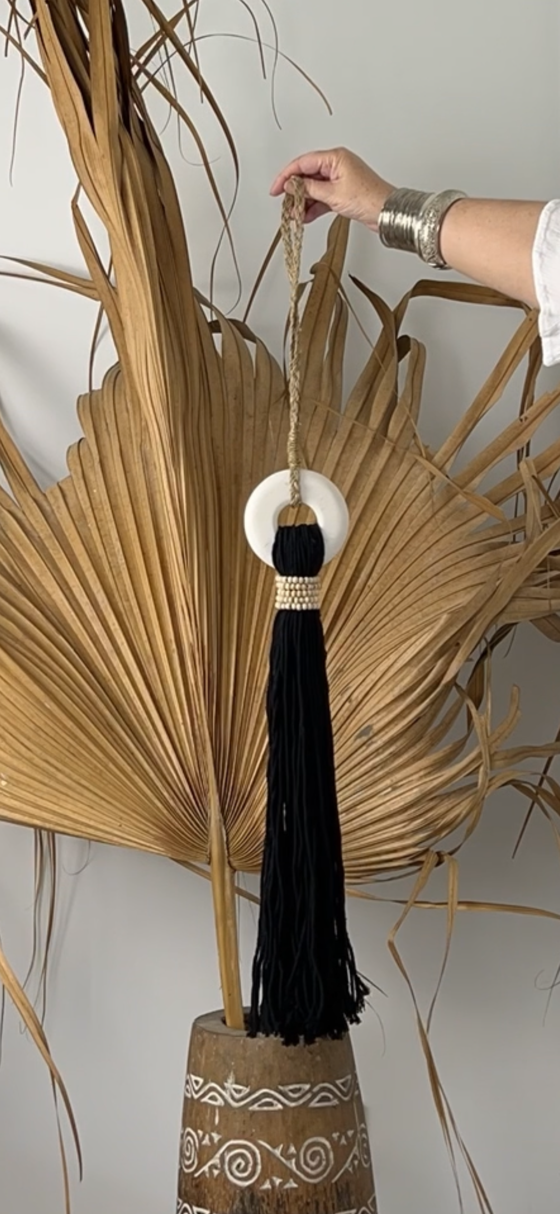 Black cotton and white marble tassel  held by a hand against a neutral  background