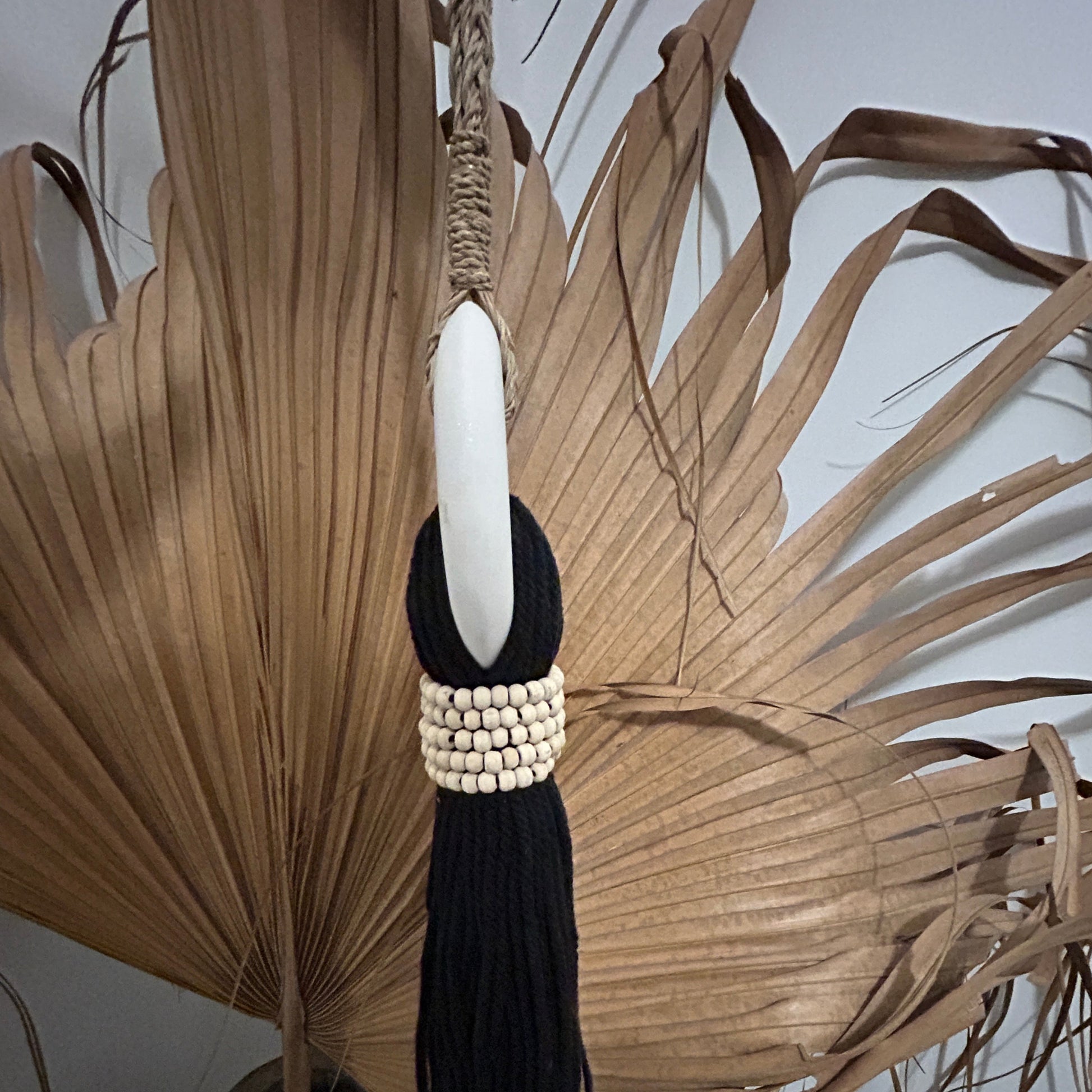 Side profile of a black cotton and white marble tassel against a palm leaf.