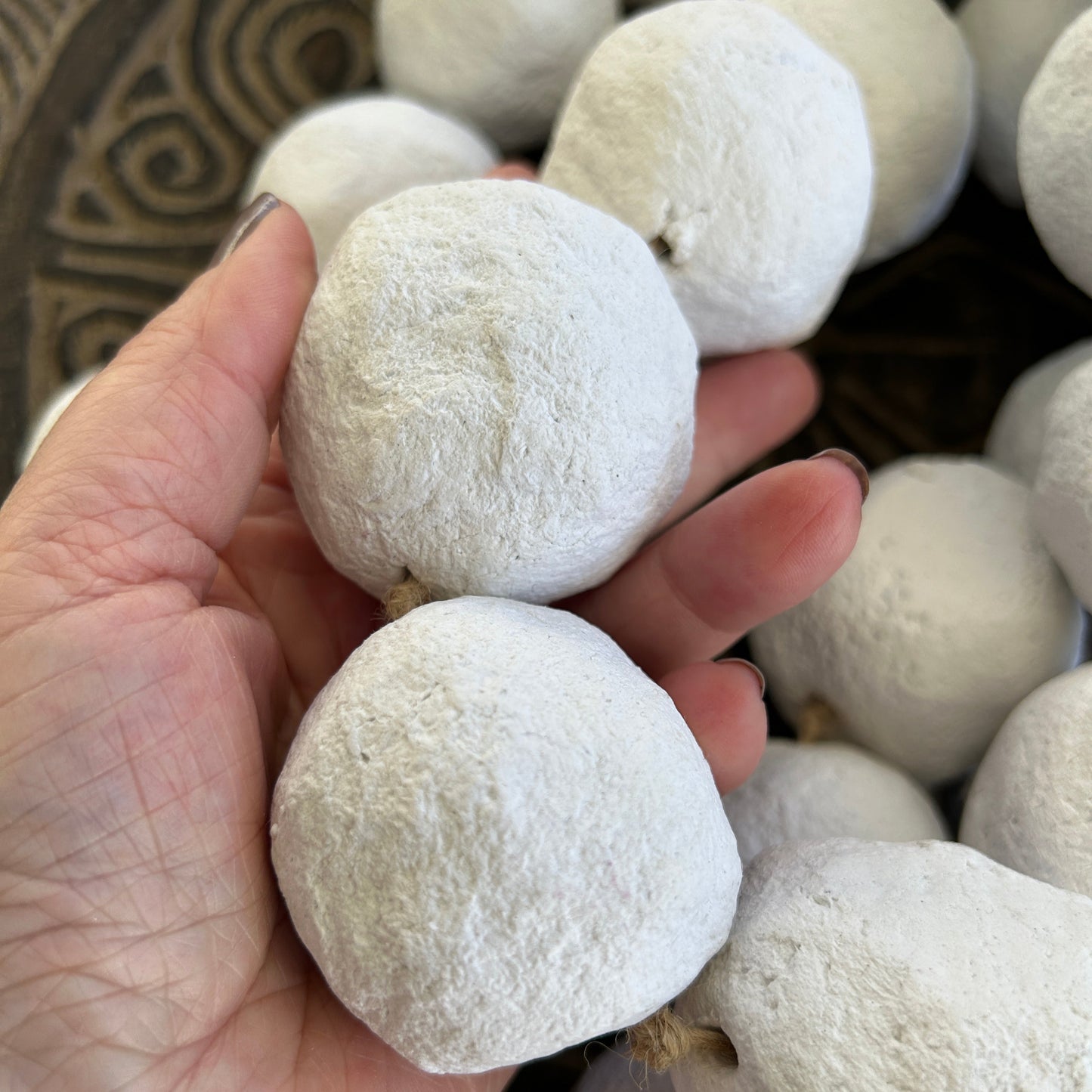Hand holding a the white extra large beaded garland to show the scale of the handmade paper mache beads.