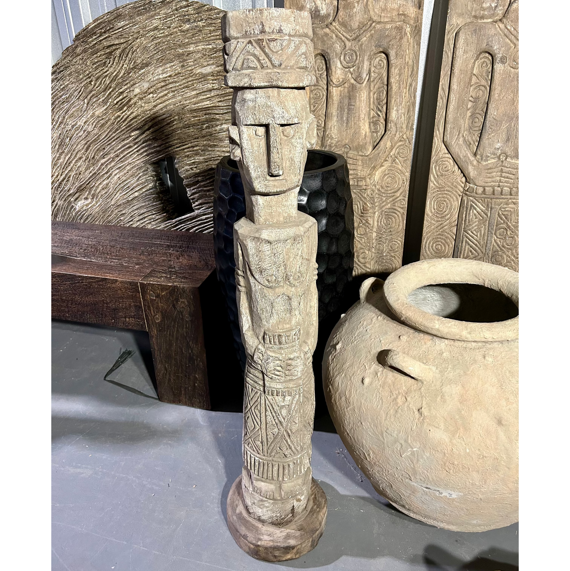 A Female Timor Ancestor statue with a human-like face and body, topped with a stylized, textured hat, displayed among other art pieces.