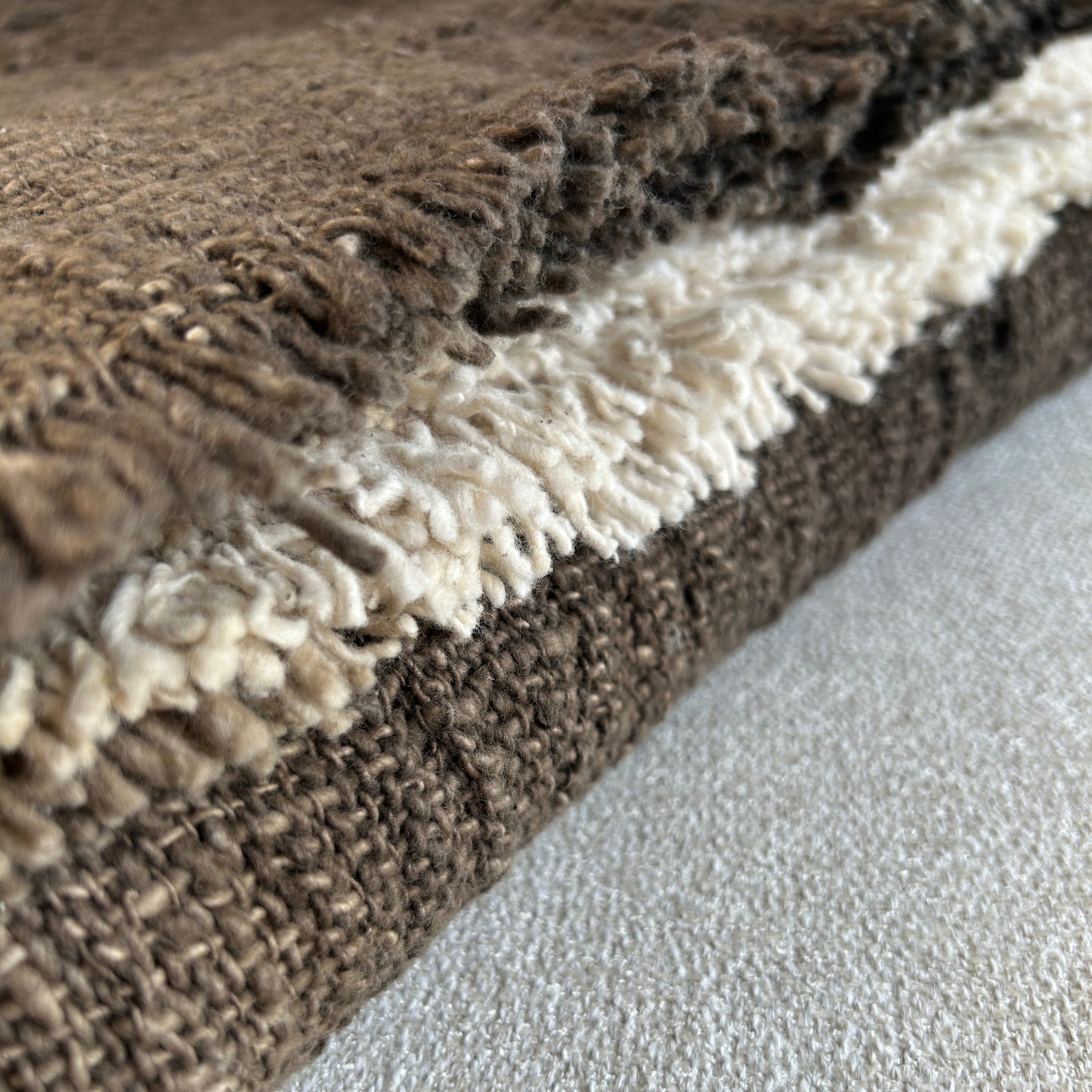 Folded cotton throw shown with fringe and woven detail close up. Rich Espresso colour of the throw set against a neutral fabric surface to highlight the depth of colour.