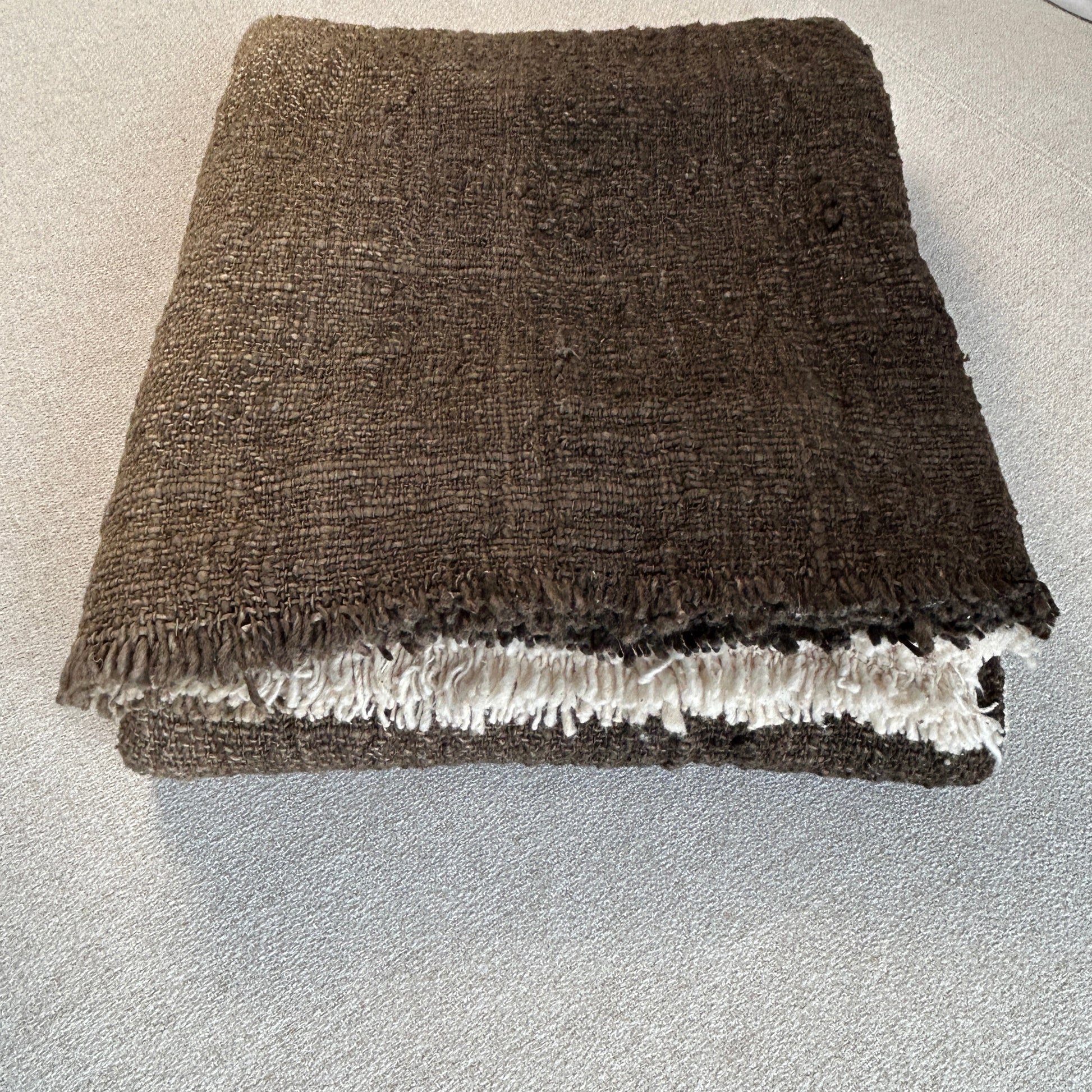 Triple folded 100% cotton throw shown with fringe and woven detail close up. Rich Espresso colour of the throw is set against a neutral fabric surface to highlight the depth of colour.