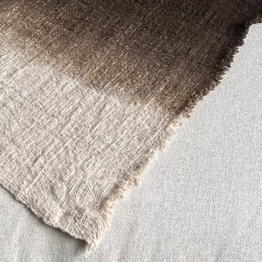 Textured image of throw laid flat showing the graduation of colour from neutral to espresso.