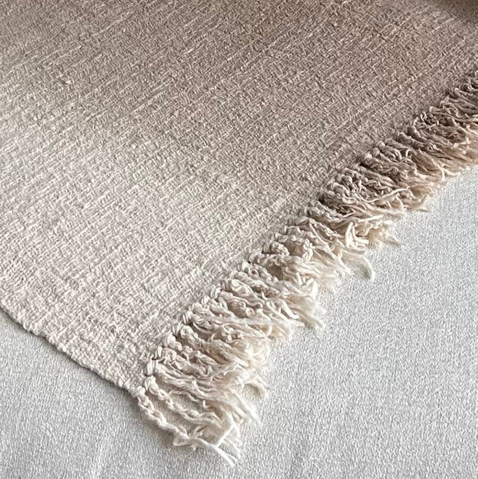 Textured blanket laid flat to show slight graduation in beige and neutral tones.