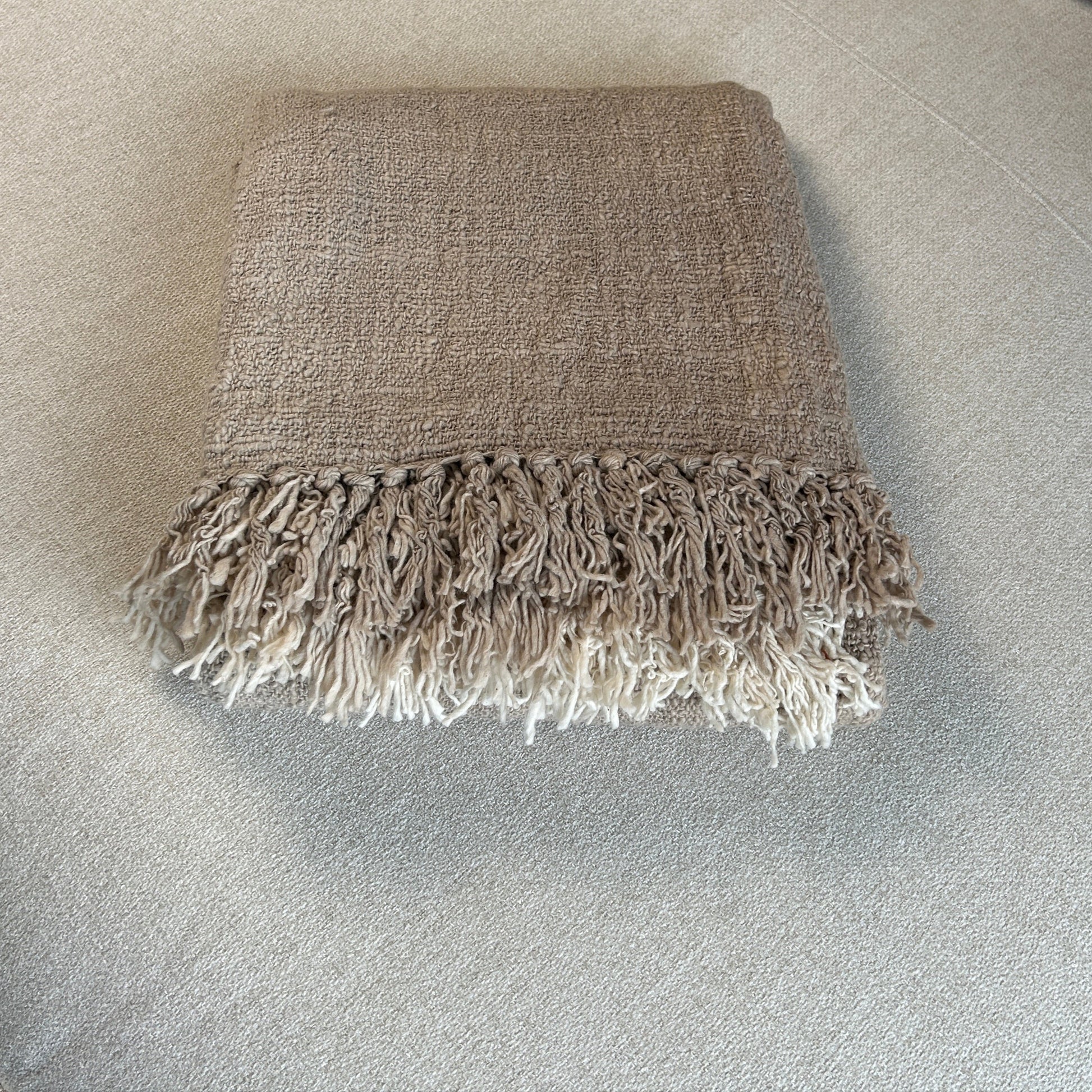 Textured blanket folded to show slight graduation in beige and neutral tones on fringe.