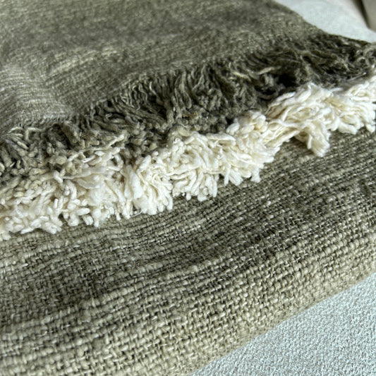 Folded cotton throw in Olive shown with olive and neutral fringe and woven detail close up. 
