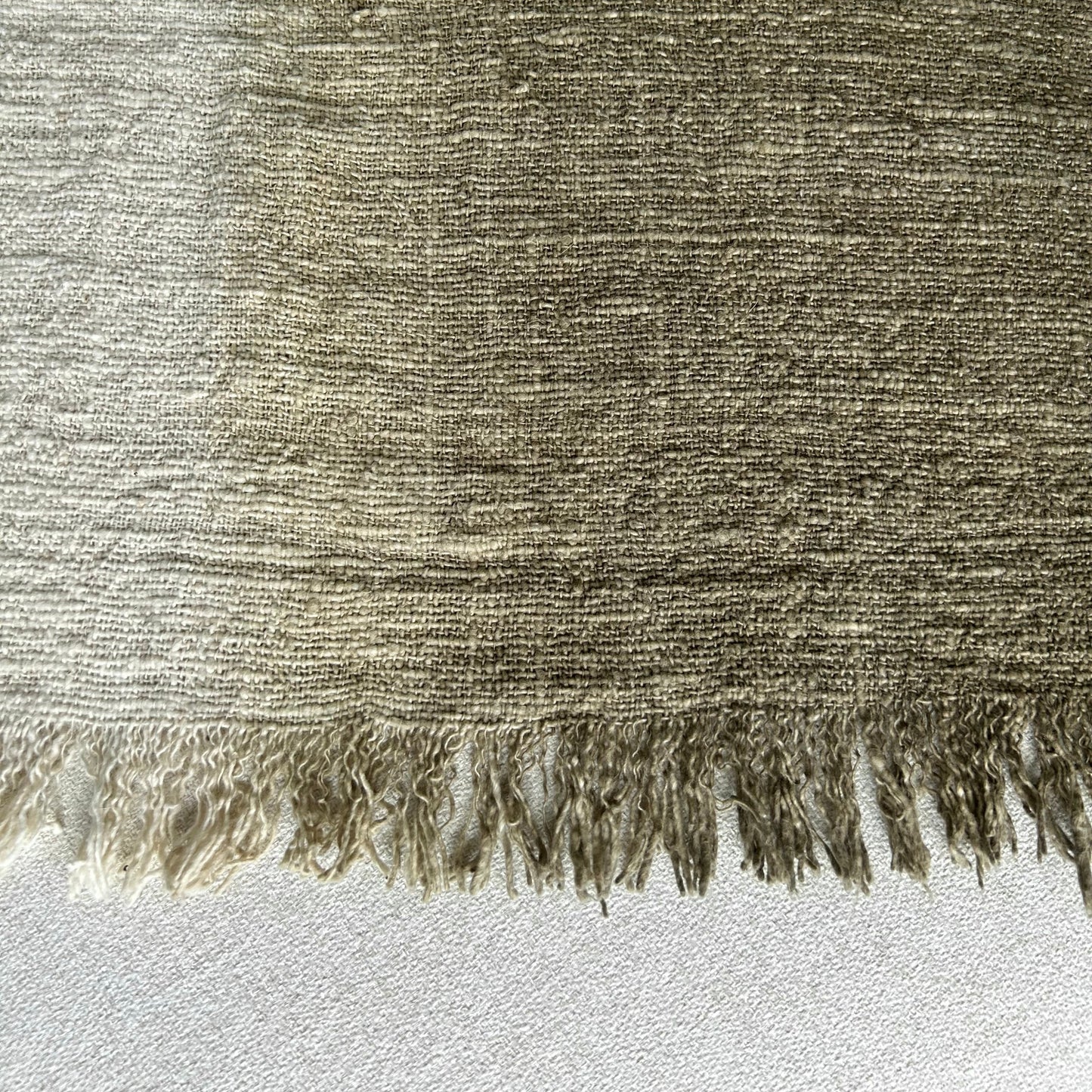 Textured fabric with frayed edge showing graduation from neutral to olive.
