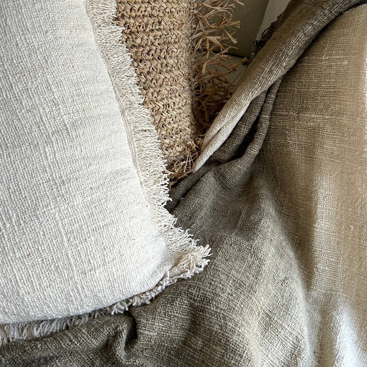 Close up details of Olive throw against a neutral handwoven cushion and raffia cushion