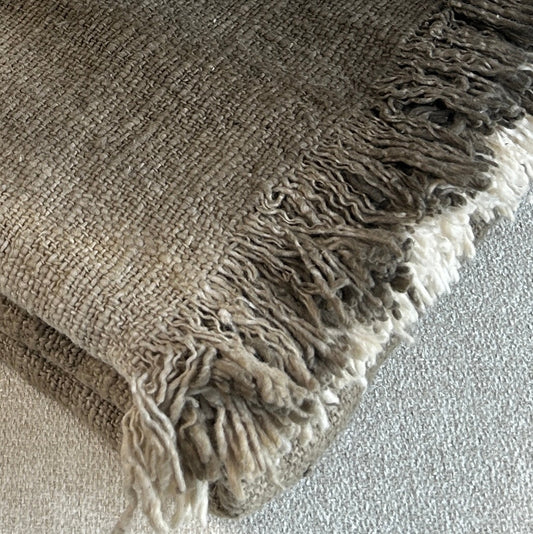 Folded cotton throw shown with fringe and woven detail close up. Rich slate colour of the throw set against a neutral fabric surface to highlight the depth of colour.