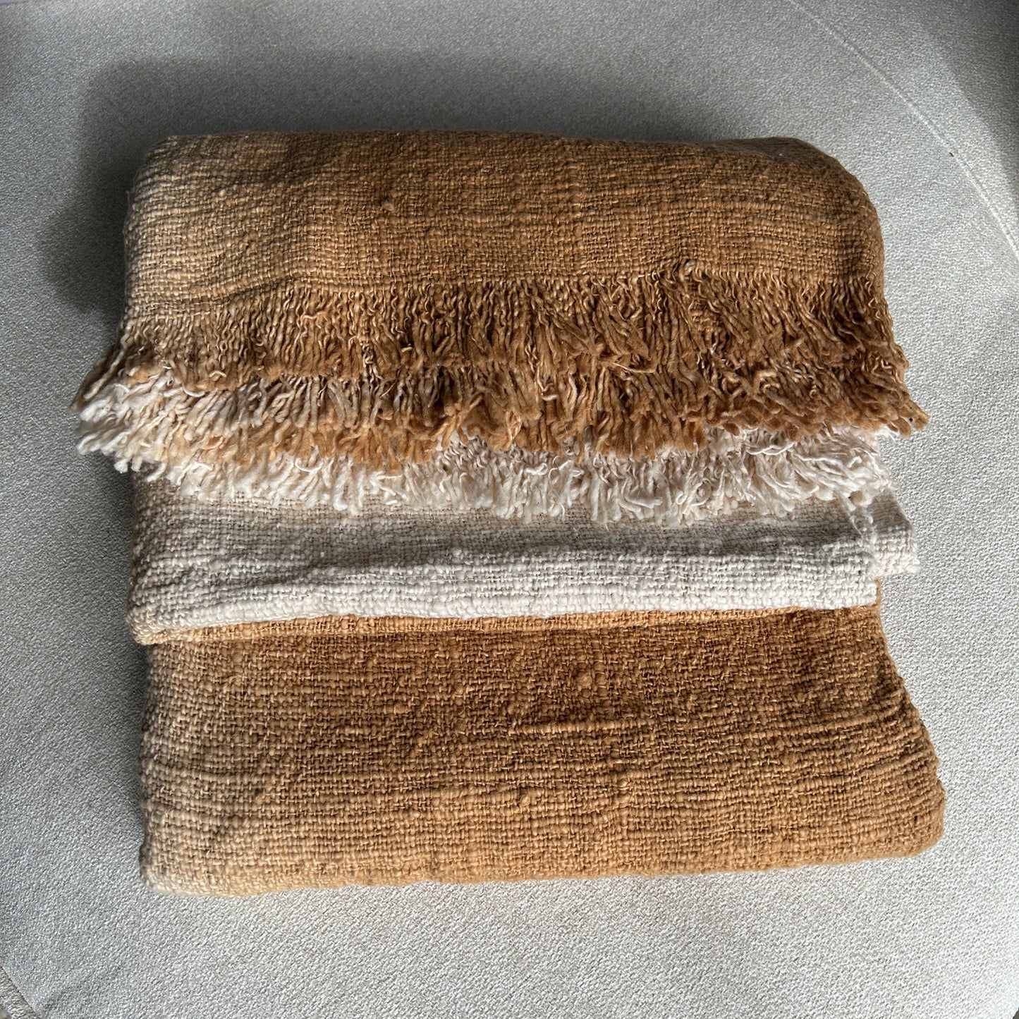 Folded image of Spice cotton throw shown with a layered fold to see the neutral off white against the Spice colourway. Golden spice colour of the throw set against a neutral fabric surface to highlight the golden tones of colour.