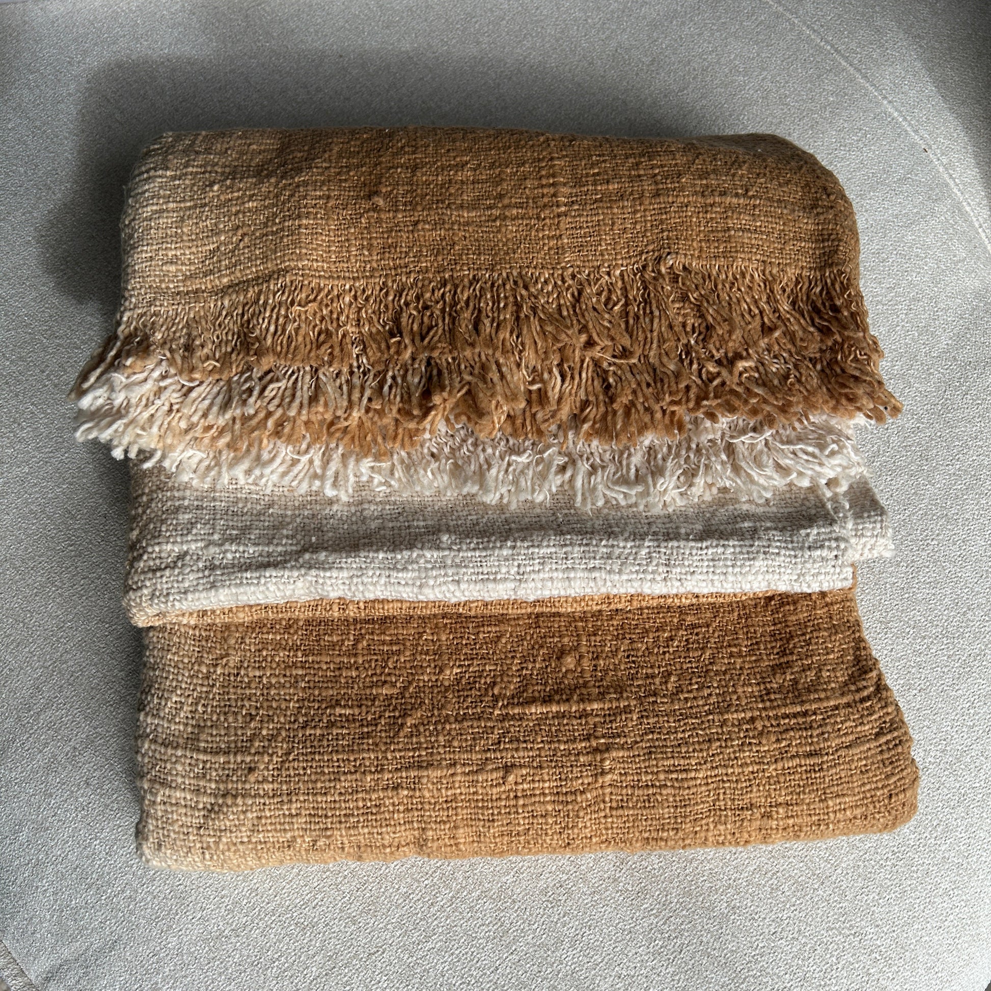 Folded image of Spice cotton throw shown with a layered fold to see the neutral off white against the Spice colourway. Golden spice colour of the throw set against a neutral fabric surface to highlight the golden tones of colour.