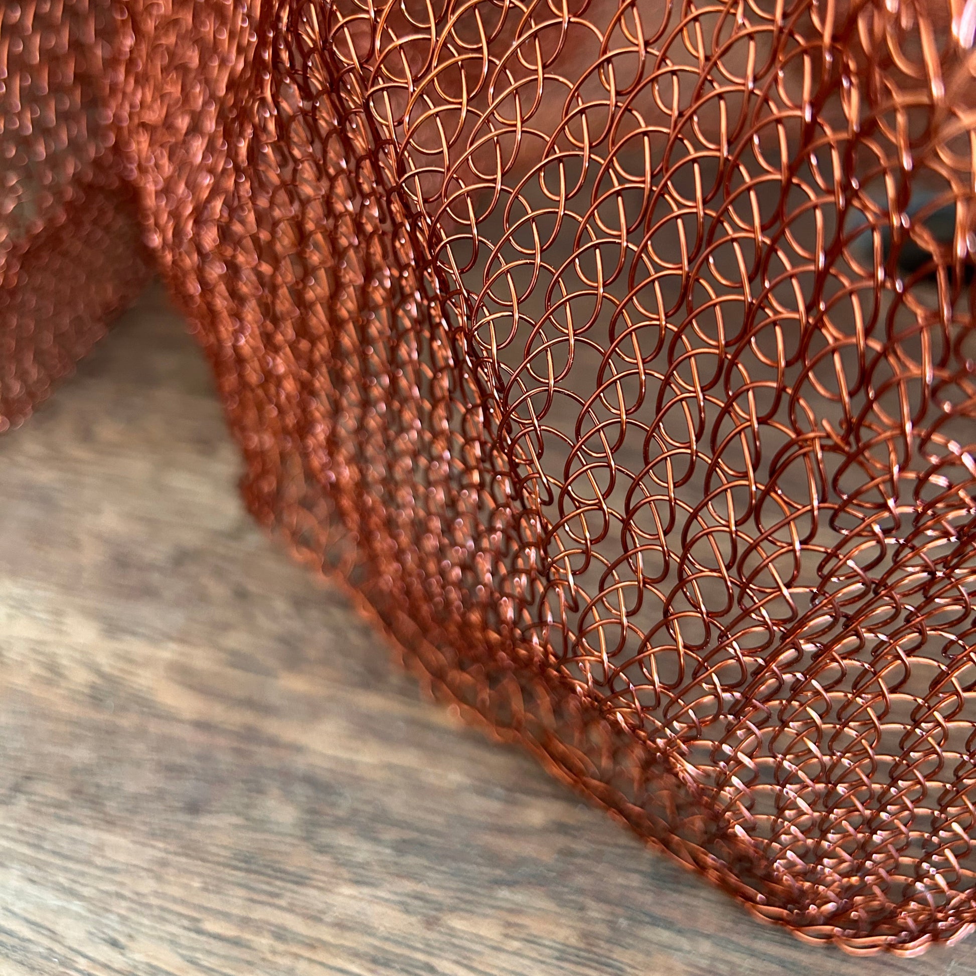 Close-up of a woven metal copper coloured mesh pendant shown on a timber table top.