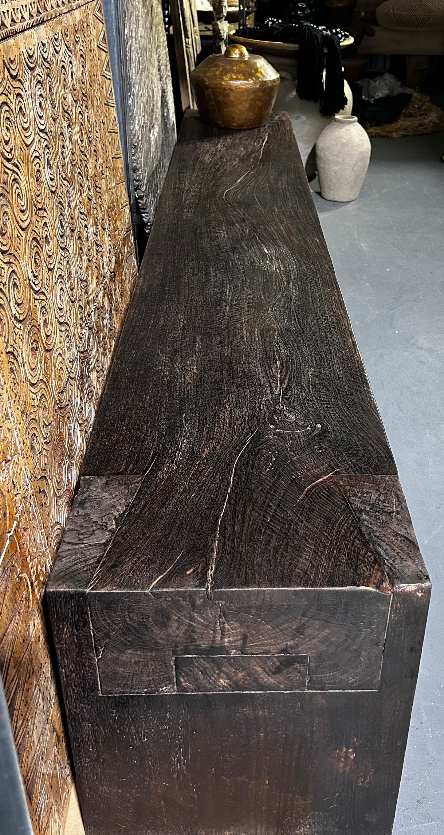 A long, dark brown timber bench seat with a distinctive grain pattern and butterfly joinery details.