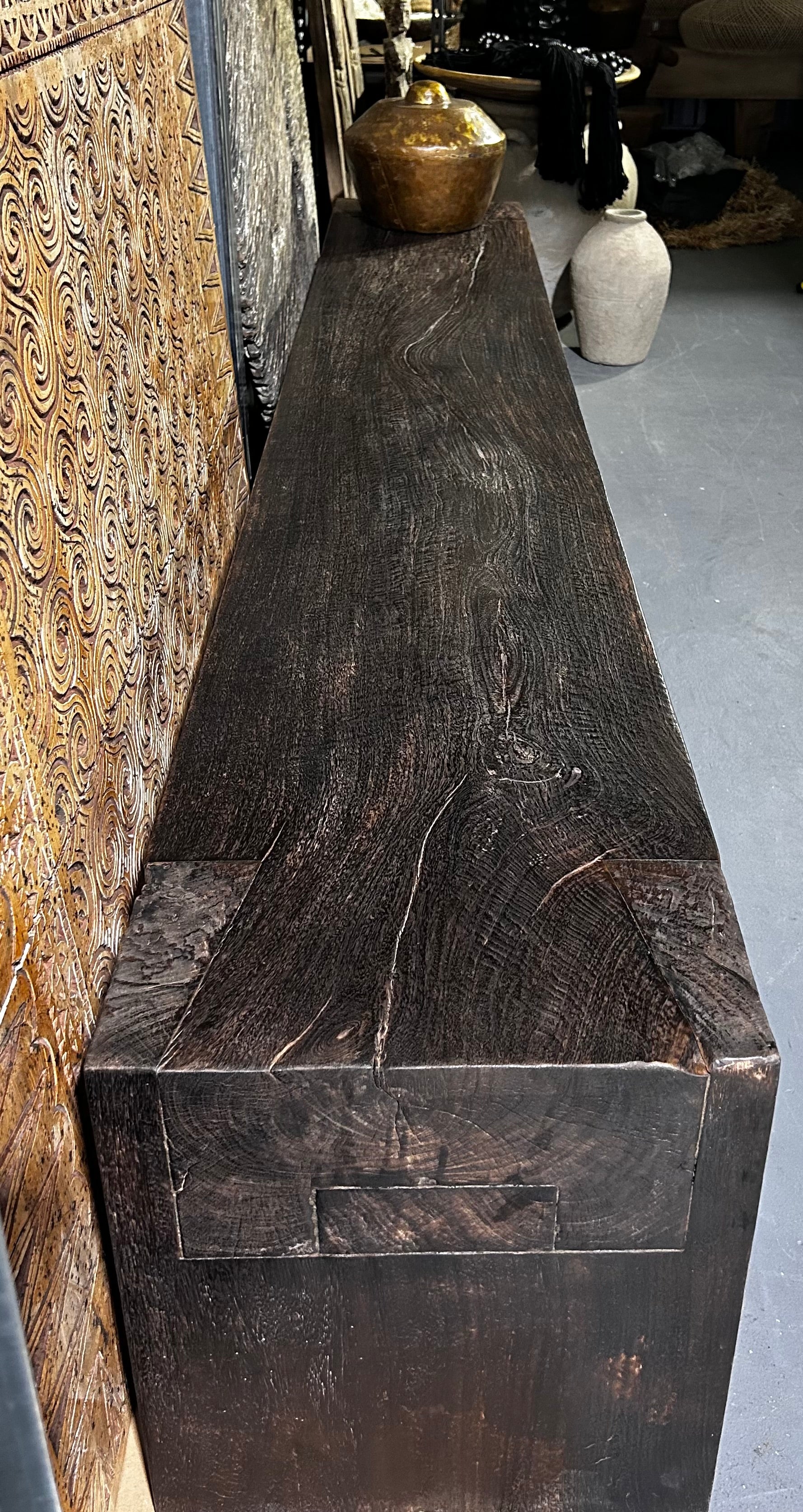 A long, dark brown timber bench seat with a distinctive grain pattern and butterfly joinery details.
