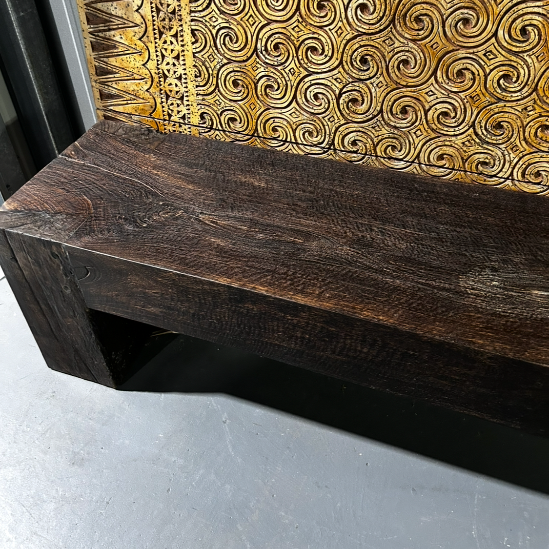Wooden bench with timber grain against a textured wall.