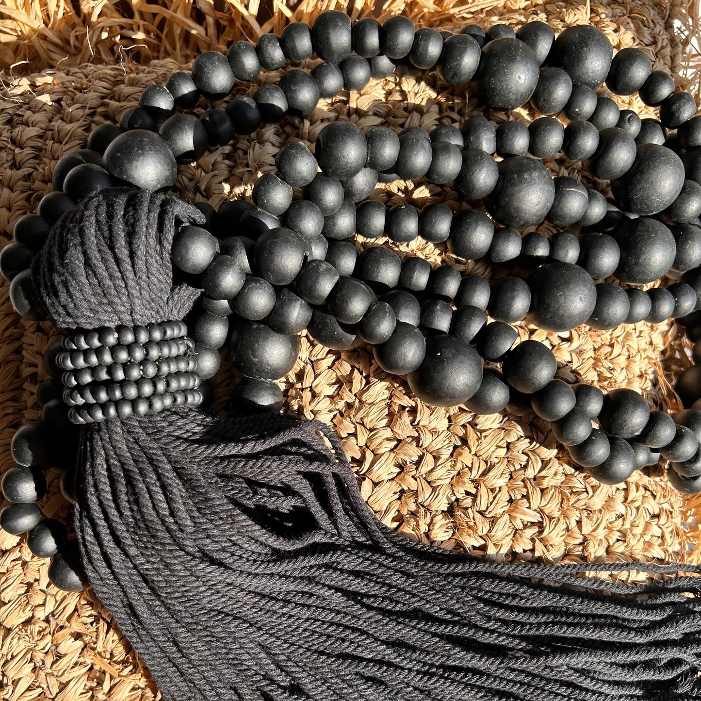 Black beaded cotton tassel shown with sunlight agains a raffia cushion cover.