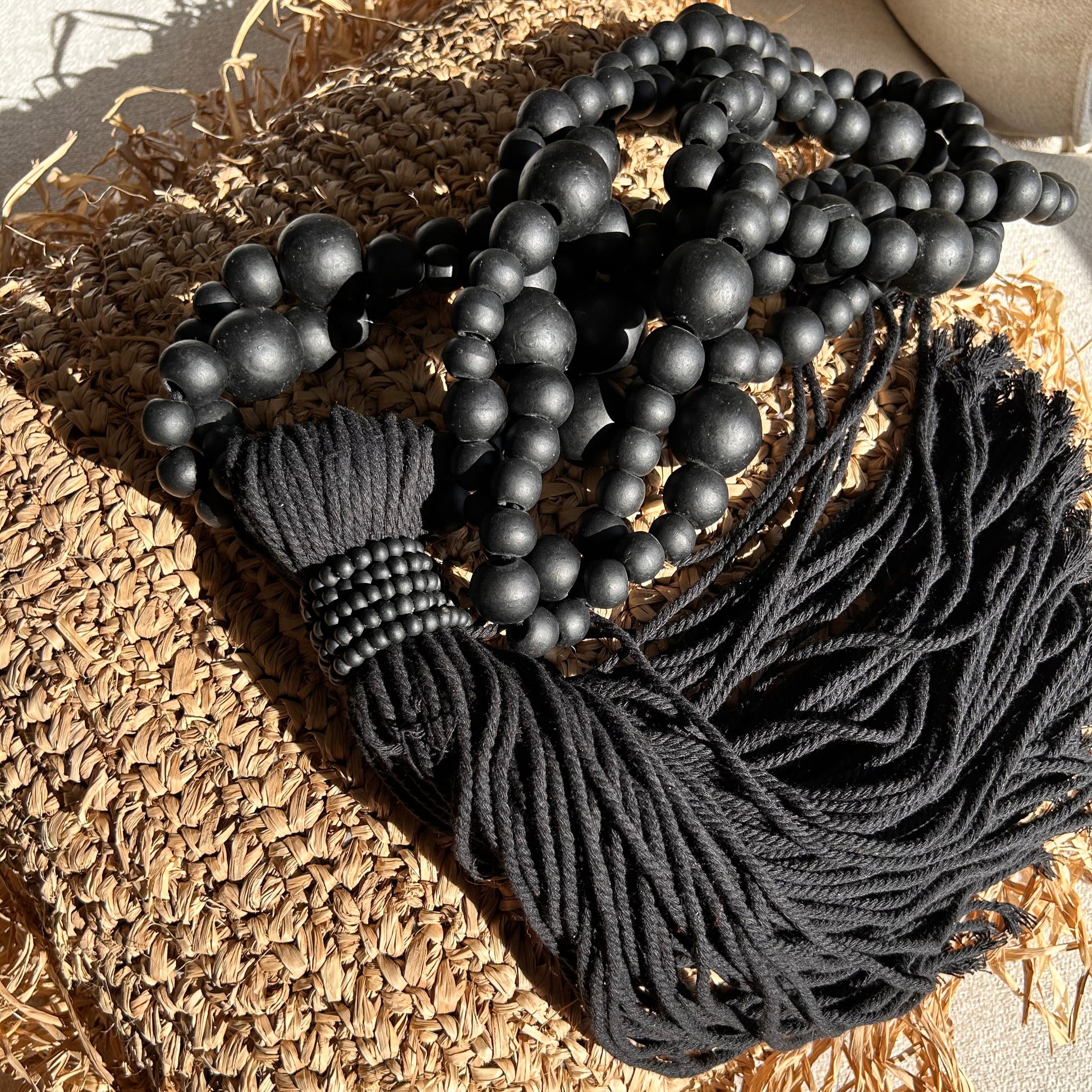 Black beaded cotton tassel on a raffia cushion in the sunlight.