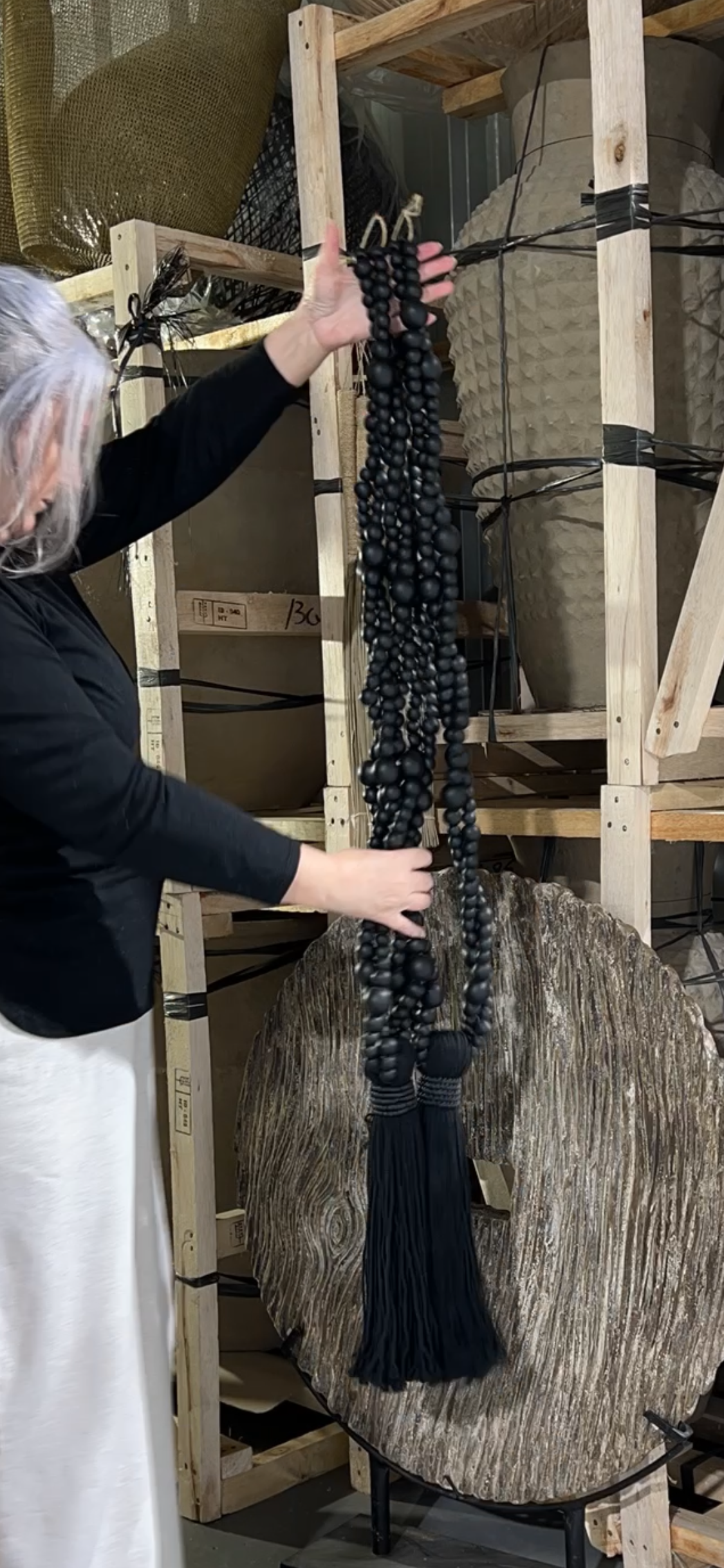 Person holding large black beaded cotton tassel in a warehouse