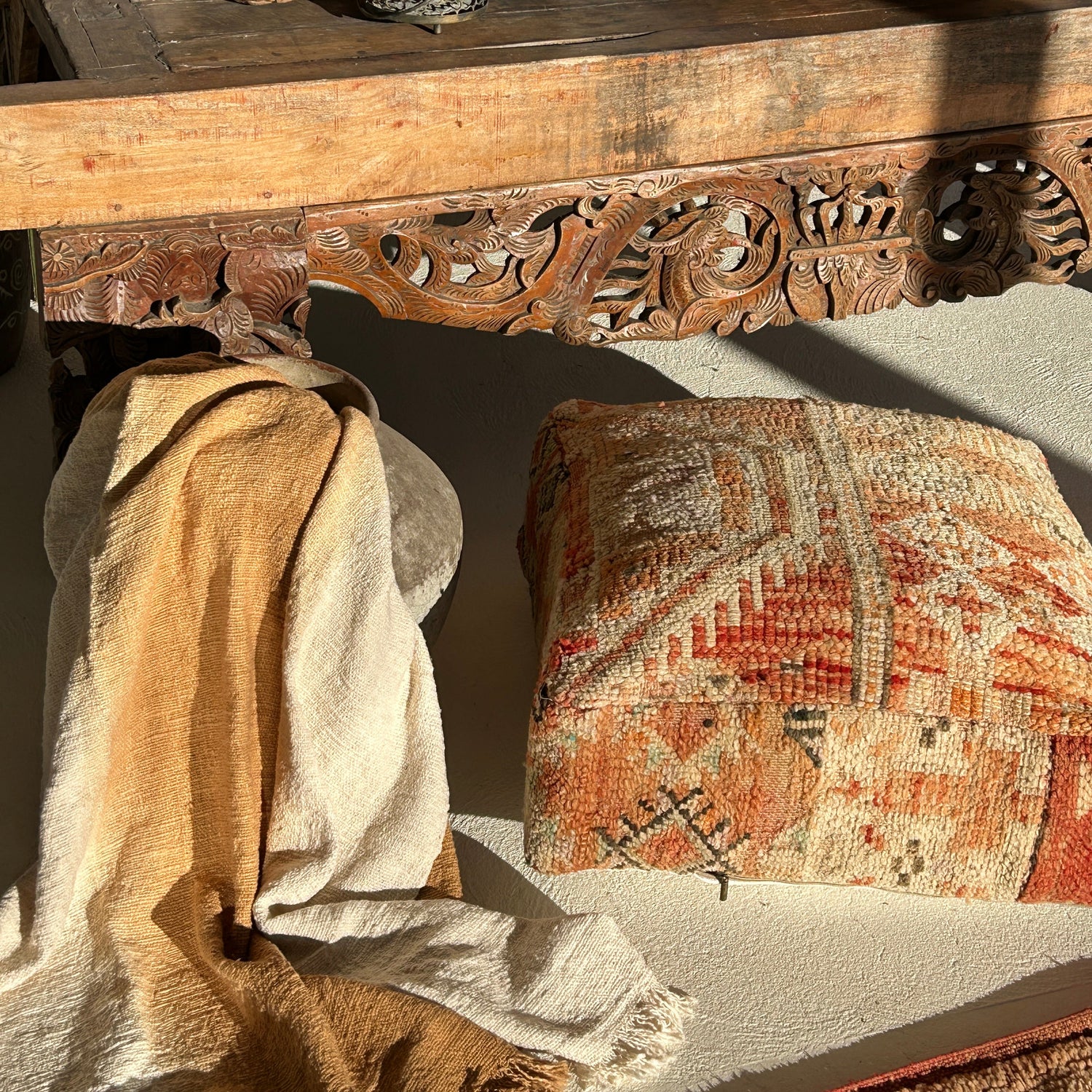 Marrakesh vintage Moroccan floor cushion featuring terracotta, cream and sand tones with geometric tribal patterns, in the sun and against off white flooring next to an Indonesian table and a pot with a mustard throw.