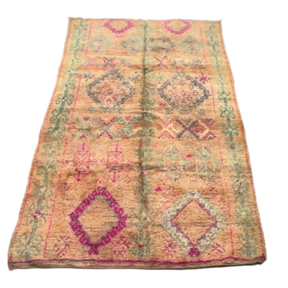 A traditional Moroccan rug with diamond shapes in magenta and teal against a pinky peach background.