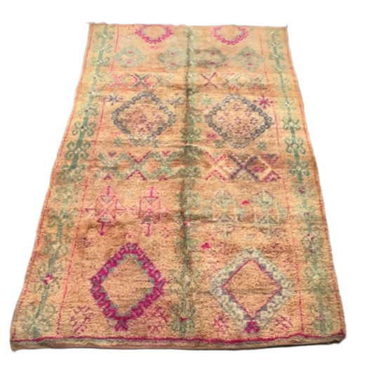 A traditional Moroccan rug with diamond shapes in magenta and teal against a pinky peach background.