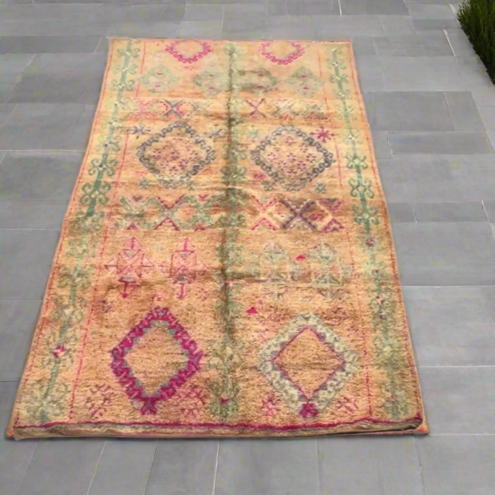 A traditional Moroccan rug with diamond shapes in magenta and teal against a pinky peach background.