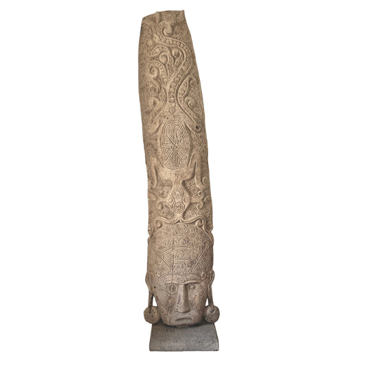A tall, slender hand-carved wooden sculpture with intricate spiral relief patterns and a pale, stone-like wash finish, standing on a grey rectangular base.