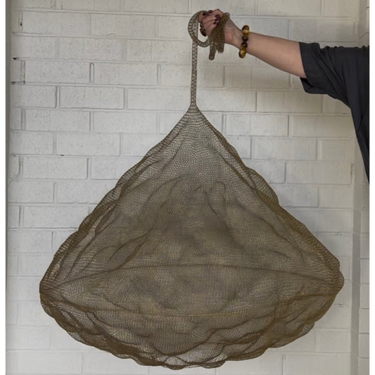 Handwoven Nomad Pendant Brass Mesh Statement Light shown against a white brick wall.