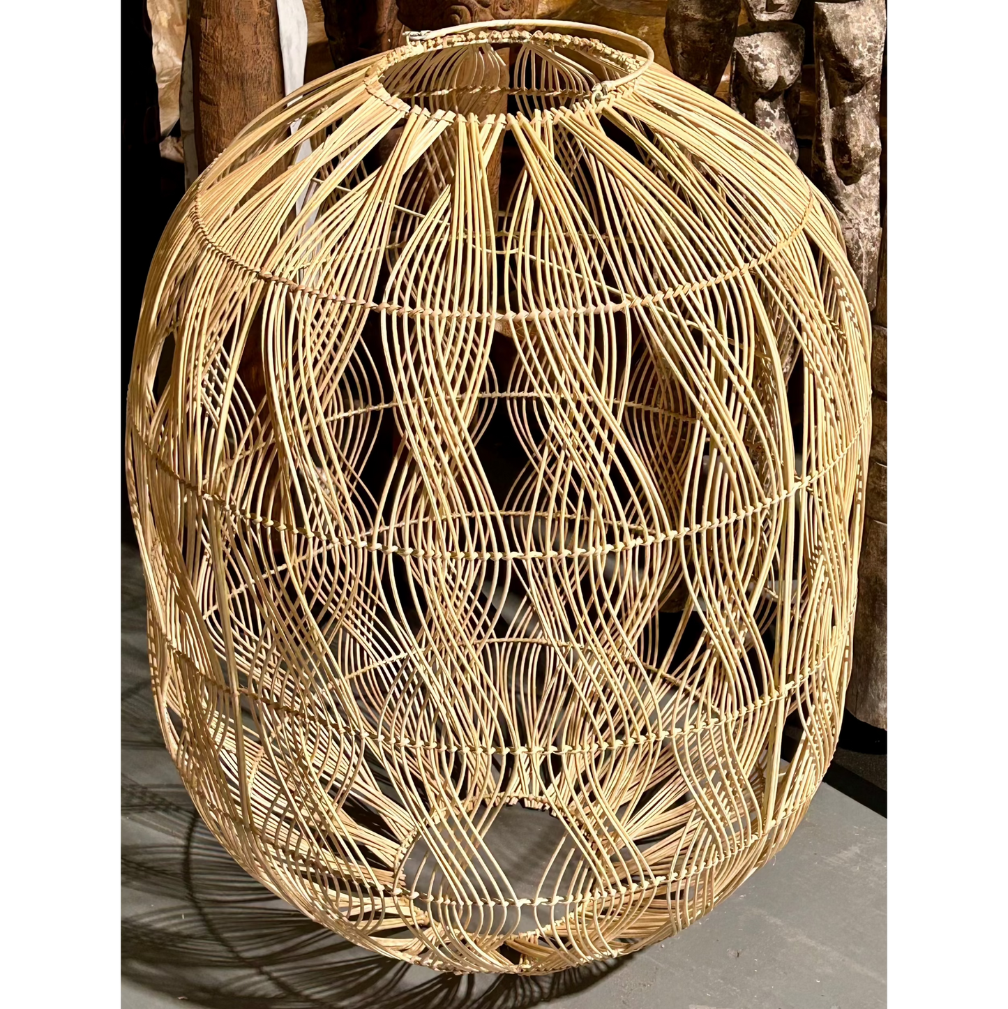 Woven rattan pendant with a vertical wave pattern on a concrete floor.