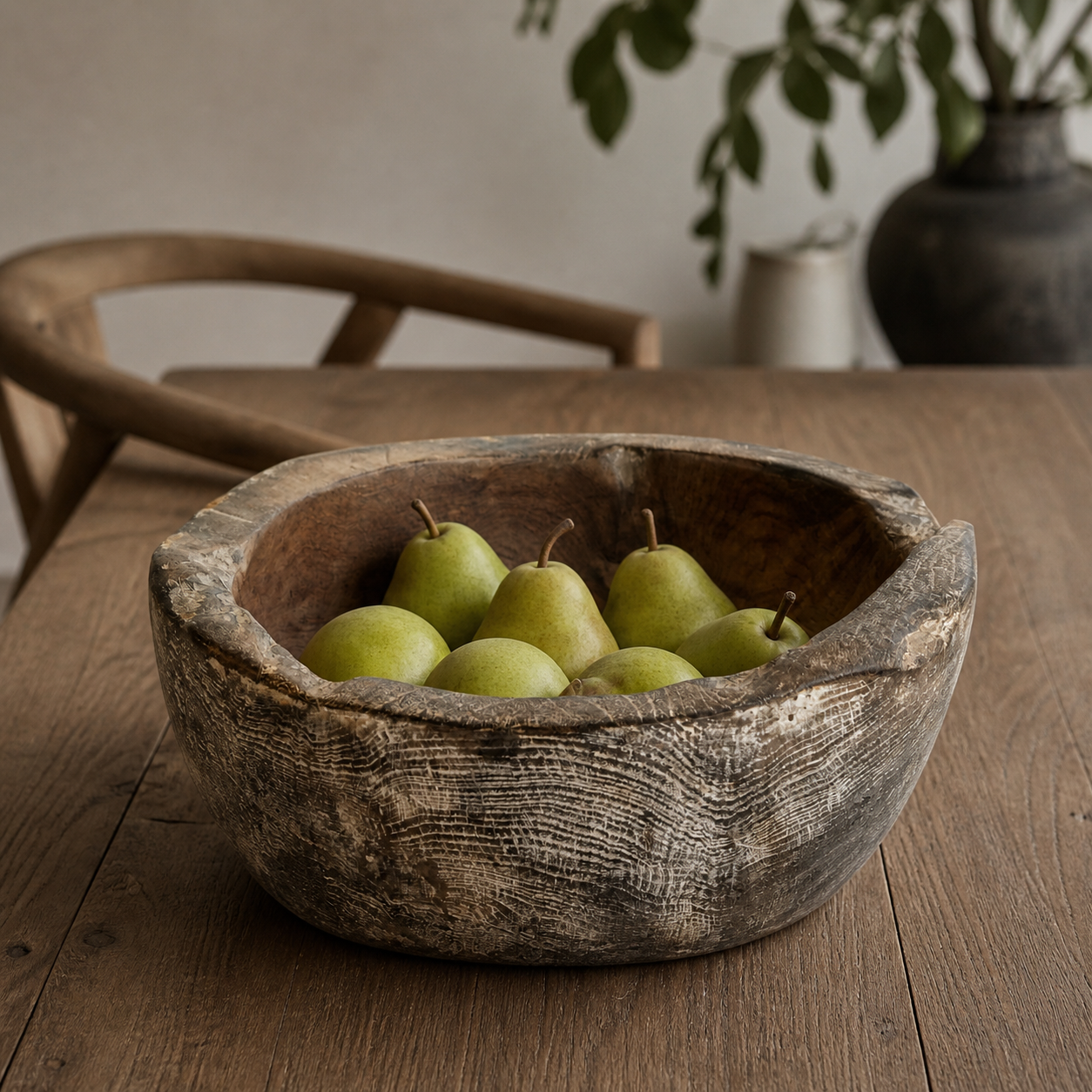 Carved teak bowl styled with green pears placed inside on a timber dining table.