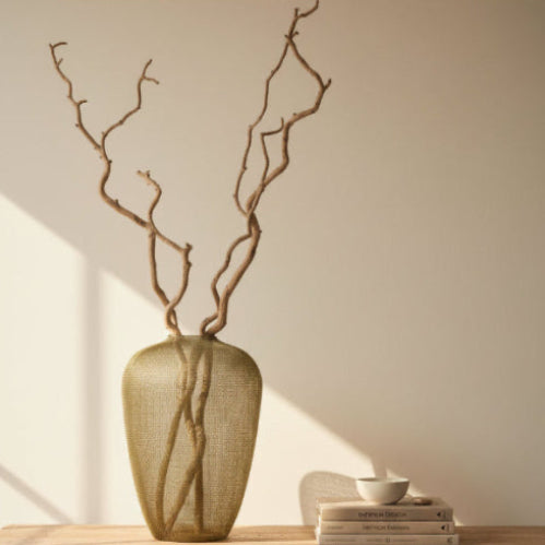 Large sculptural urn made of hand-crocheted antique gold wire standing on a light-coloured tiled floor.