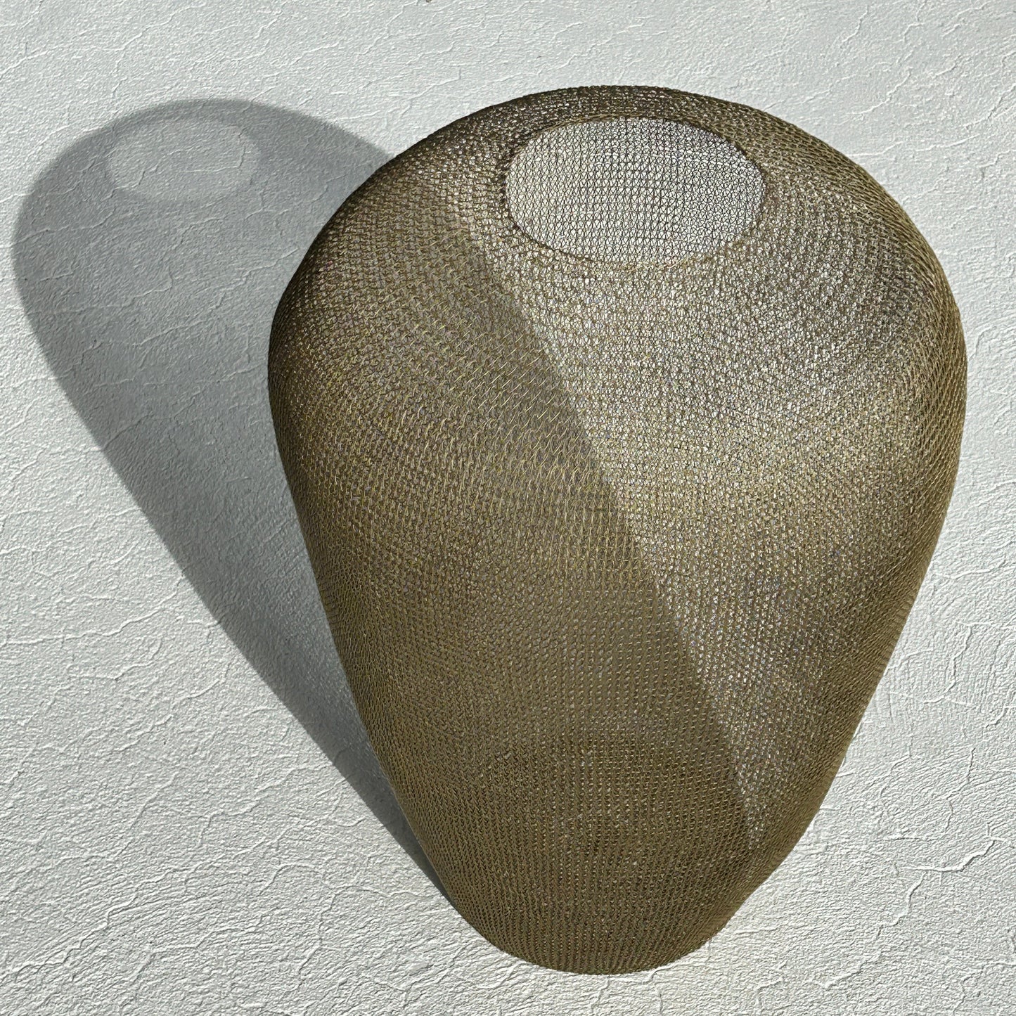 Large 60cm sculptural urn made of hand-crocheted antique gold wire standing on a light-colored tiled floor.