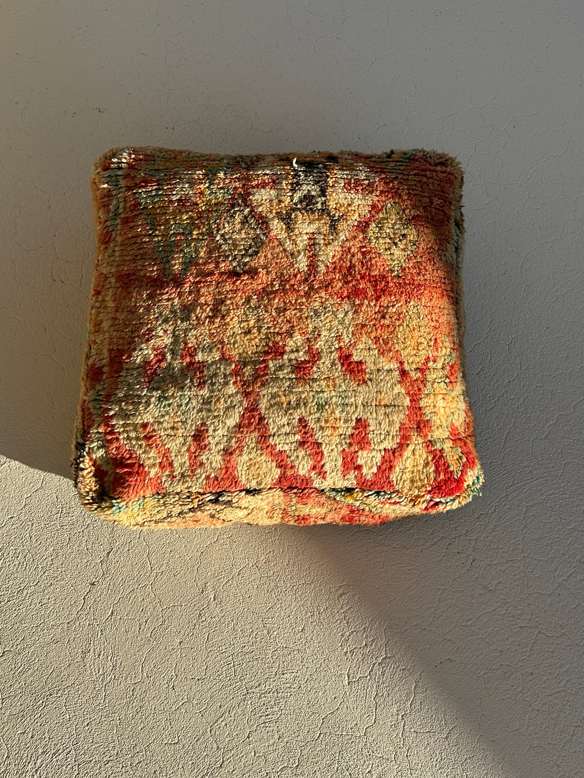 Spice vintage Moroccan floor cushion featuring warm terracotta, saffron and sage tones, handcrafted textile sourced from Morocco shown against an off white background in afternoon sunlight.
