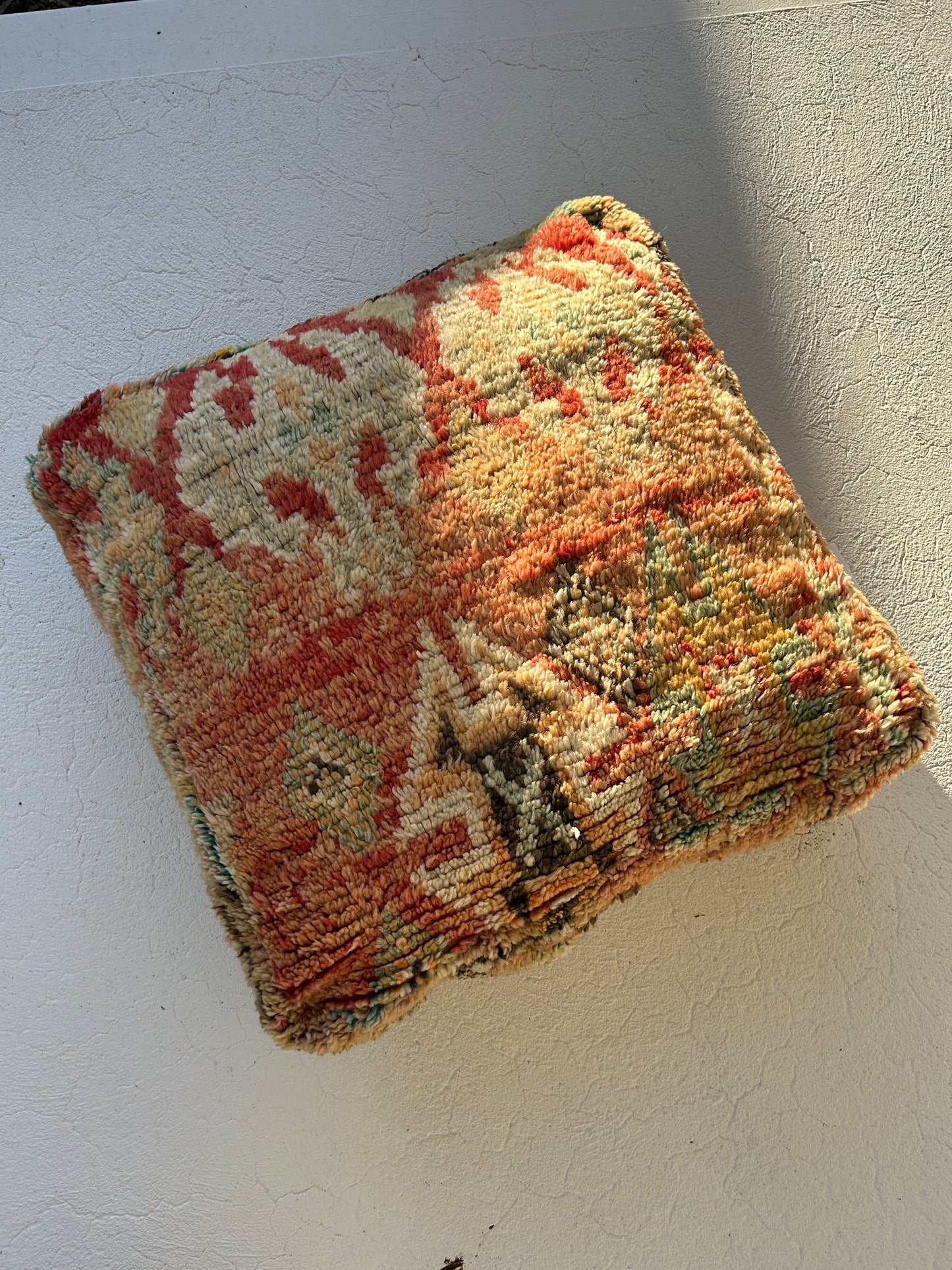 Spice vintage Moroccan floor cushion featuring warm terracotta, saffron and sage tones, handcrafted textile sourced from Morocco shown against an off white floor, half bathed in afternoon sunlight.