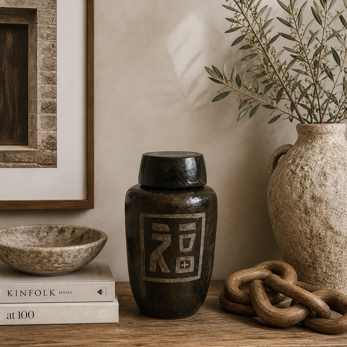 Handmade dark clay Indonesian jar with a lid featuring a hand-etched Chinese 'Fu' blessing symbol styled on a shelf with books, bowl and pot.
