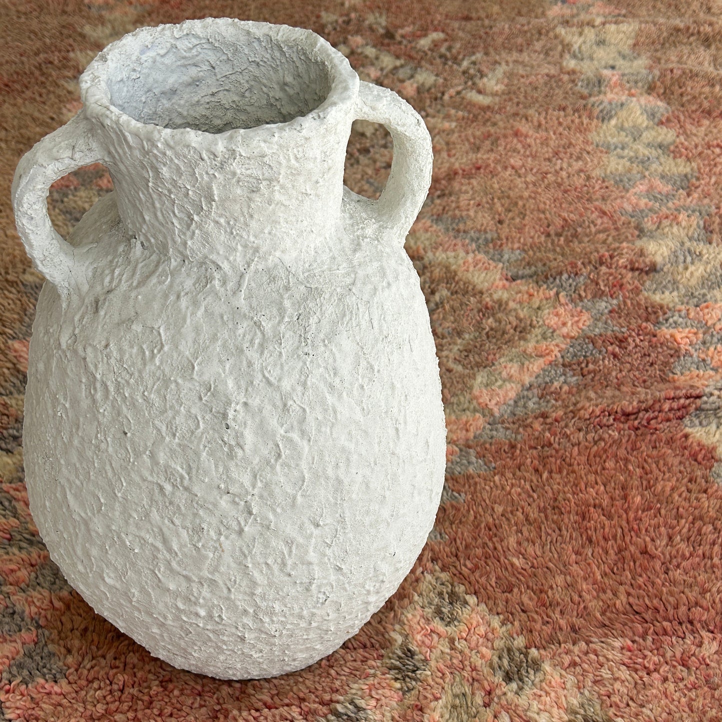 White textured vase on a patterned Moroccan rug background.