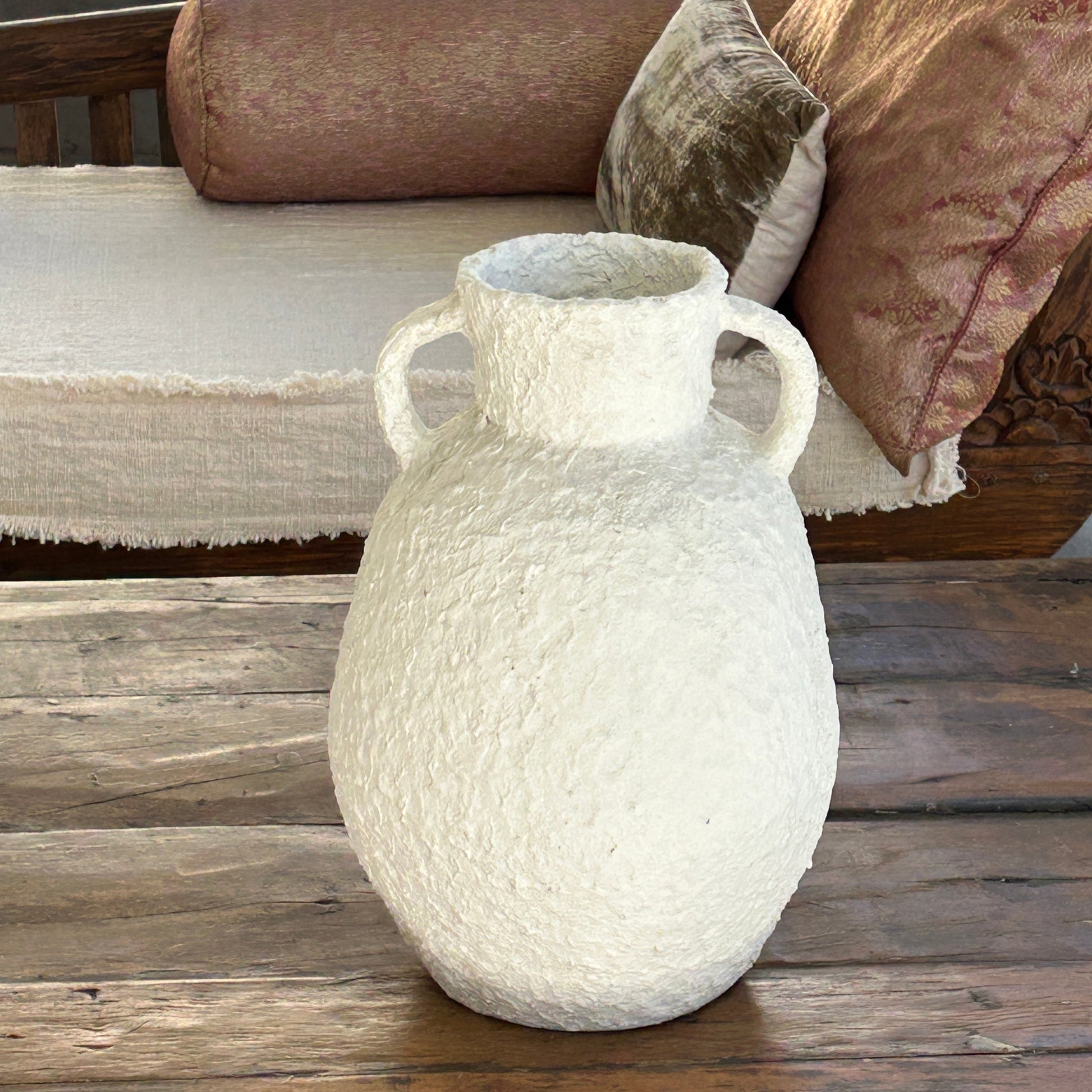 Textured white vase on a wooden coffee table with cushions in the background