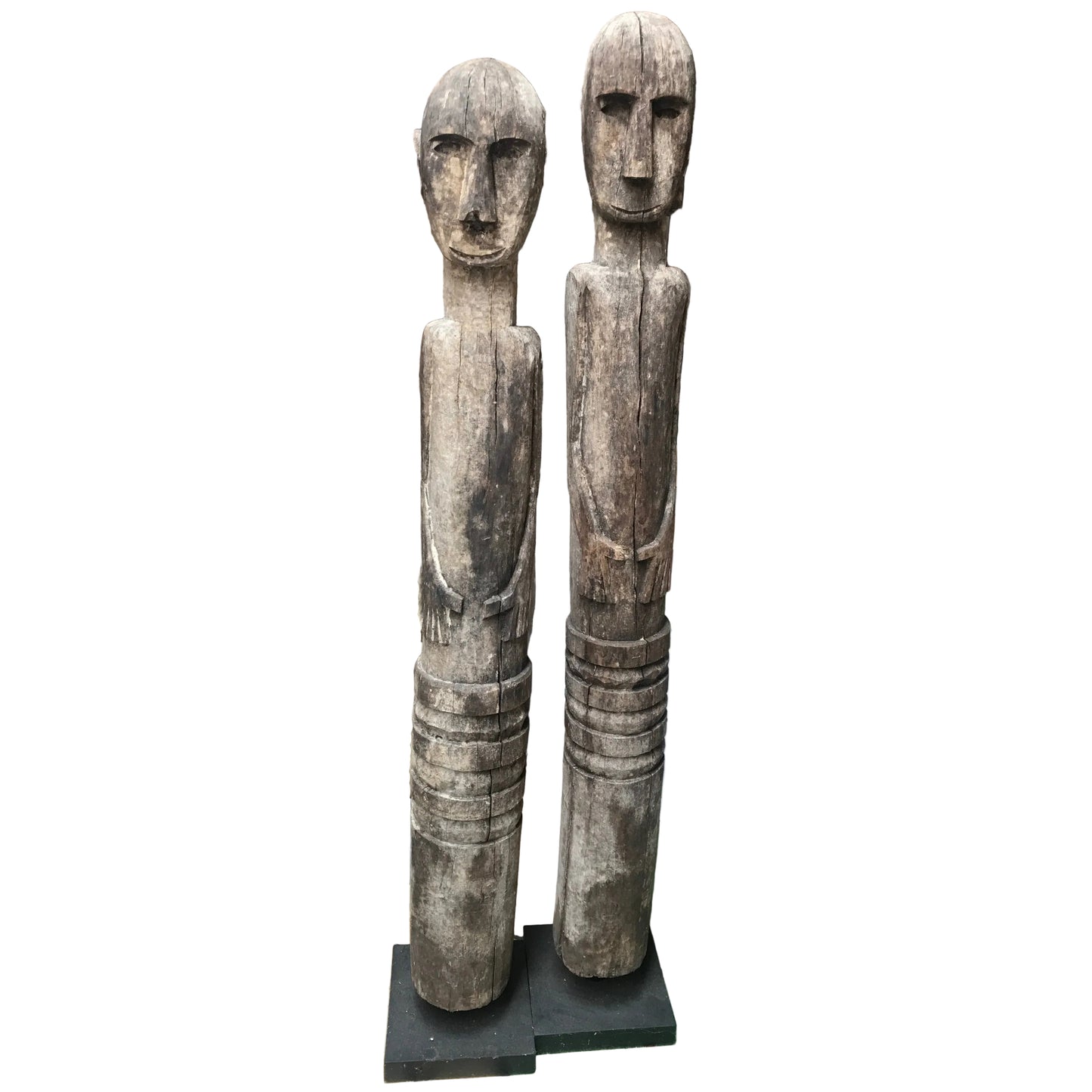 Hand-carved wooden Timor ancestor statues on black museum stands, measuring 107cm and 112cm, featuring primitive faces and weathered wood.