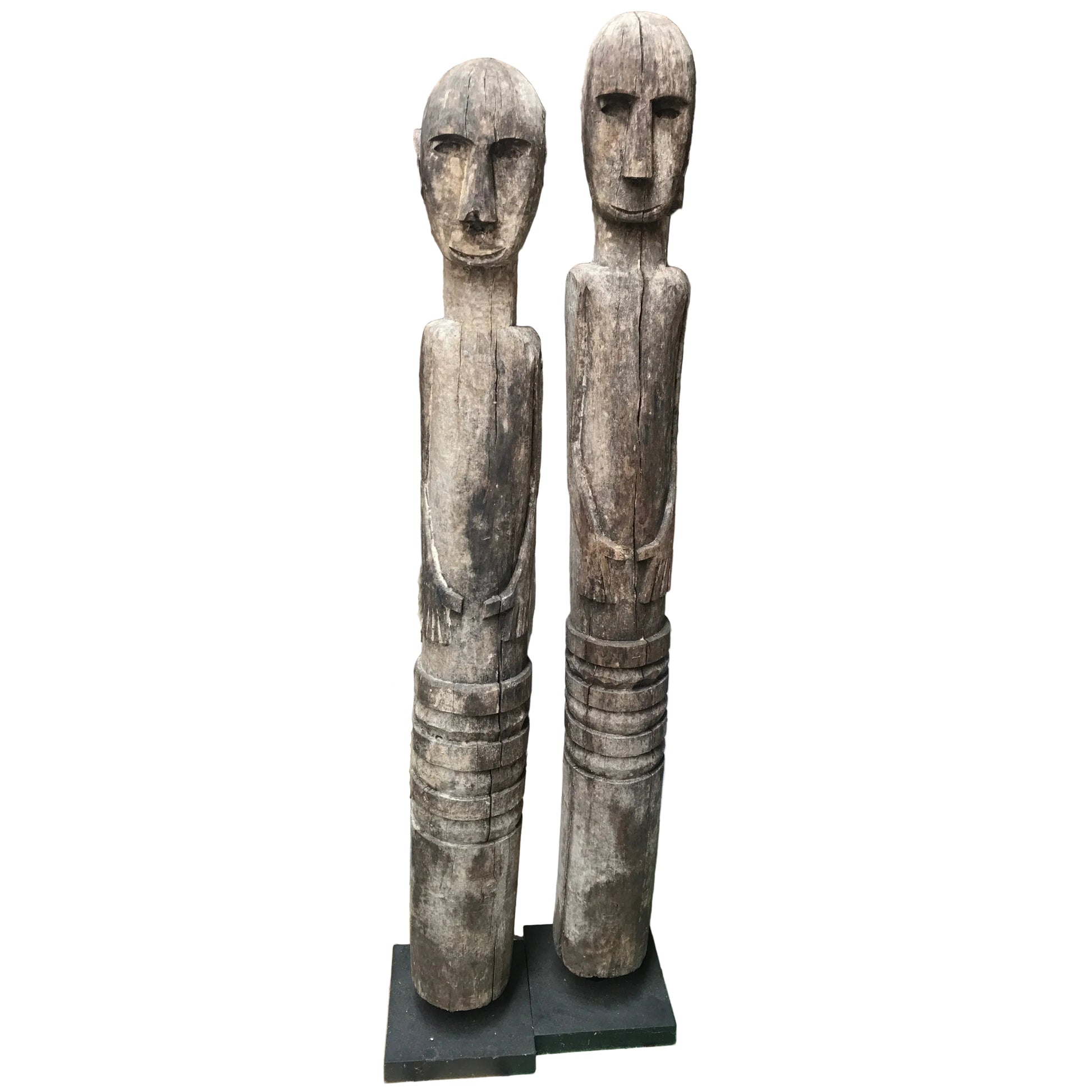Hand-carved wooden Timor ancestor statues on black museum stands, measuring 107cm and 112cm, featuring primitive faces and weathered wood.