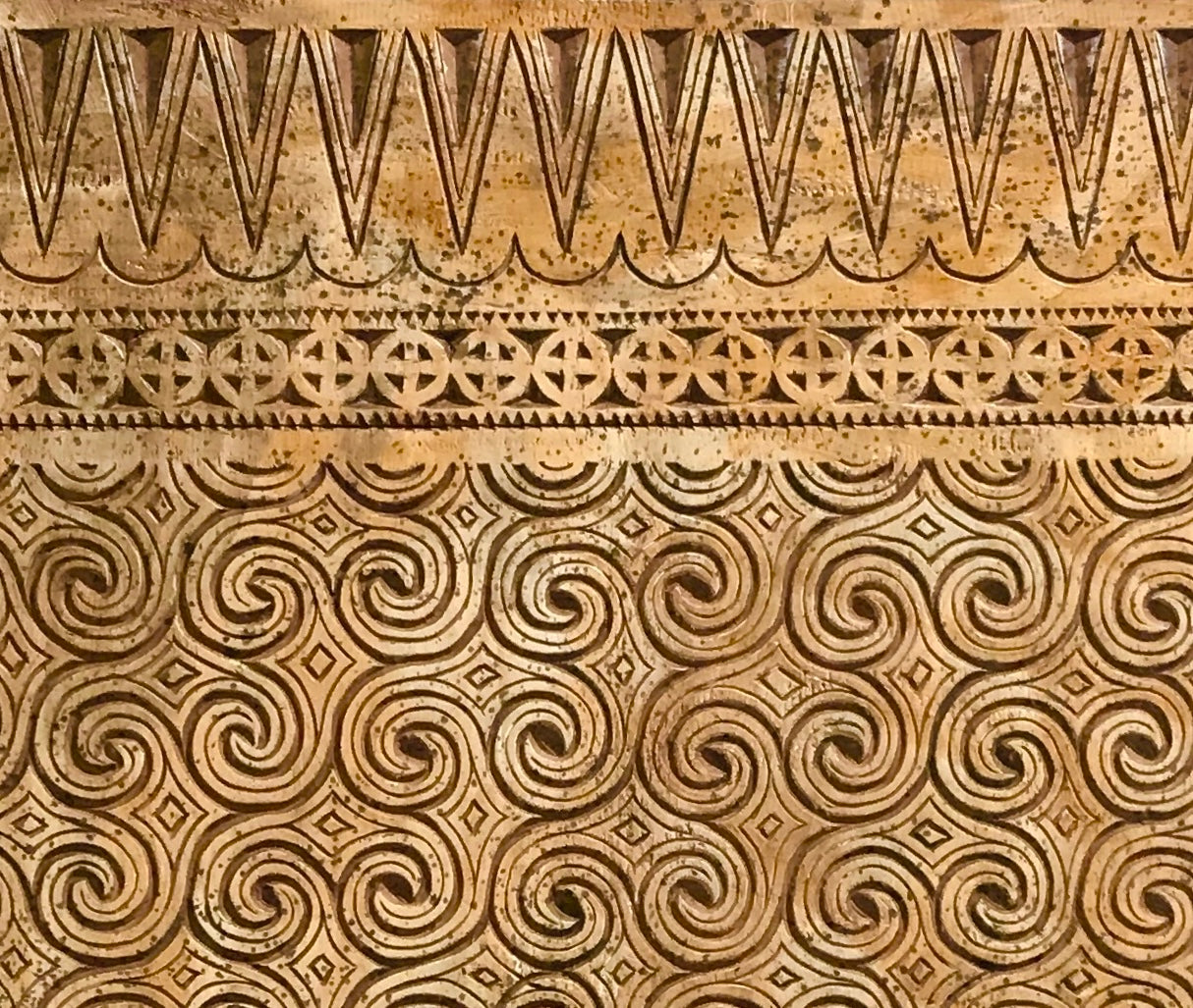 Closeup image of hand carved swirl pattern in timber panel.