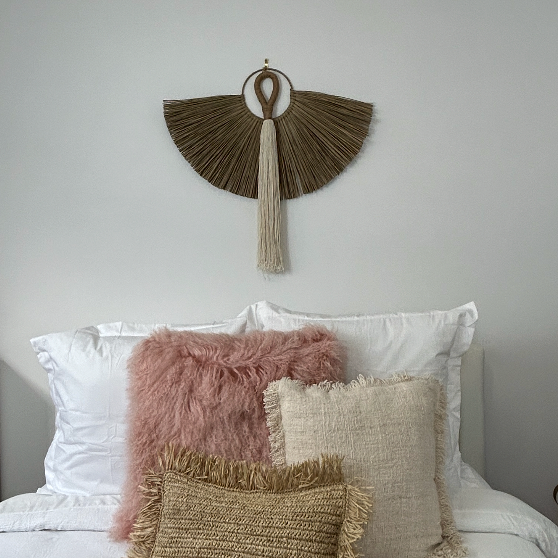 The white cotton and jute tassel shown styled above above a bed with pillows