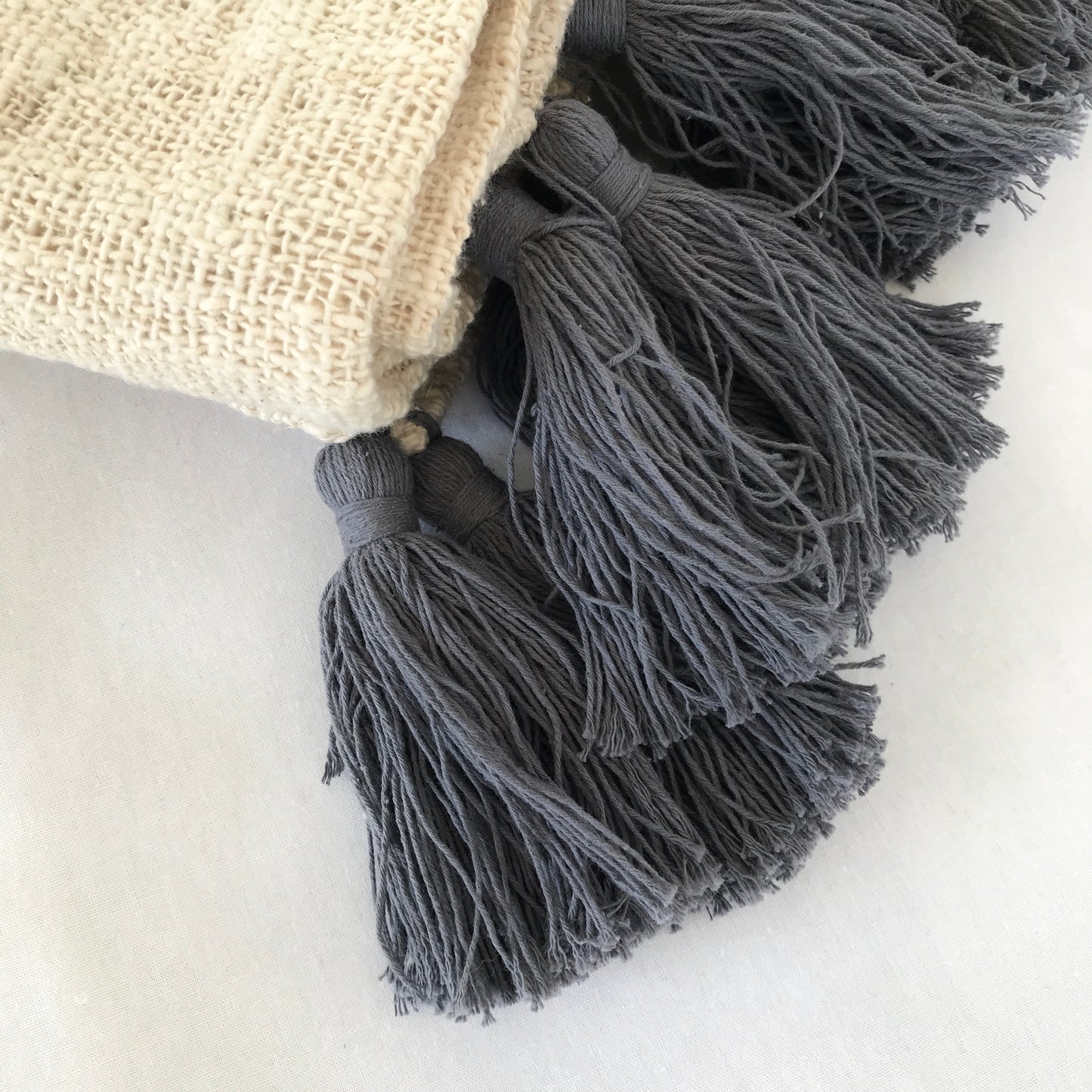 Close up of a natural cotton blanket with grey tassels folded on a white surface